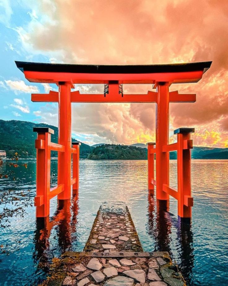 an orange gate sitting on top of a body of water next to a stone walkway