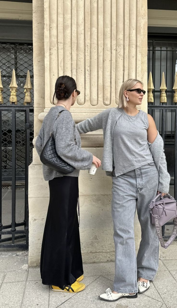 two women standing next to each other in front of a stone column with columns behind them