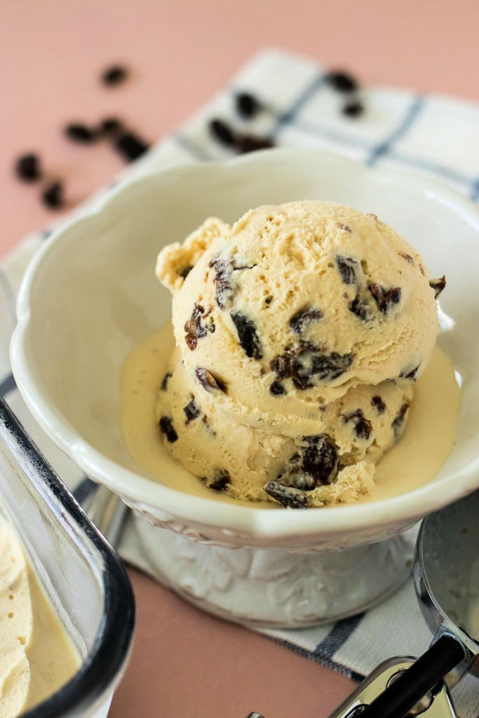 two scoops of ice cream with raisins on top in a white bowl