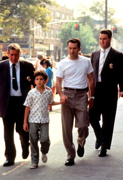 two men and a little boy walking down the street with other people on either side