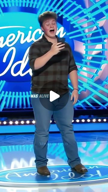 a man standing on top of a stage with his hands in his pockets and an american idol logo behind him