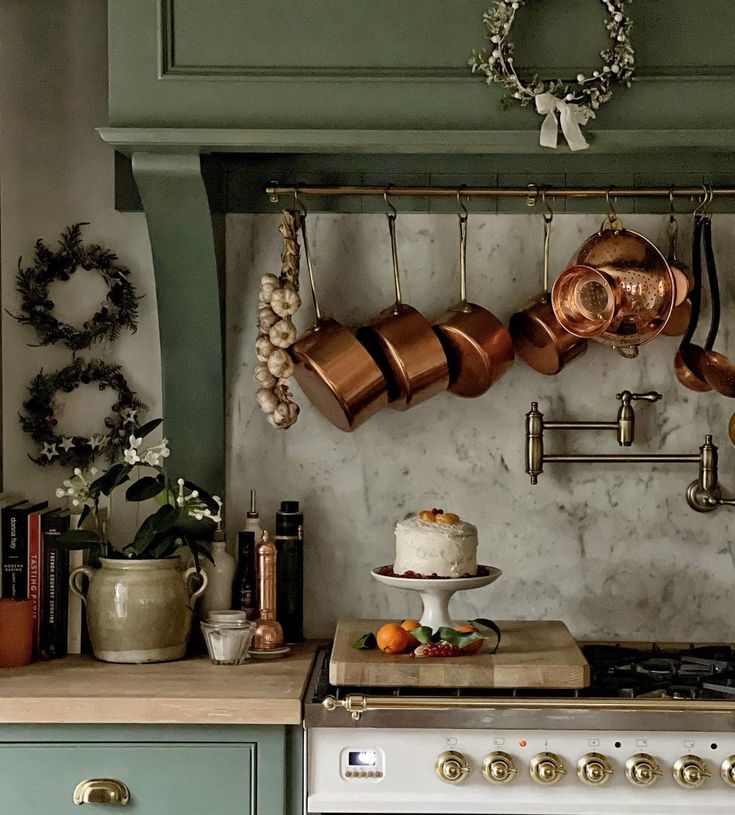 pots and pans are hanging on the wall above an oven in a kitchen with green cabinets