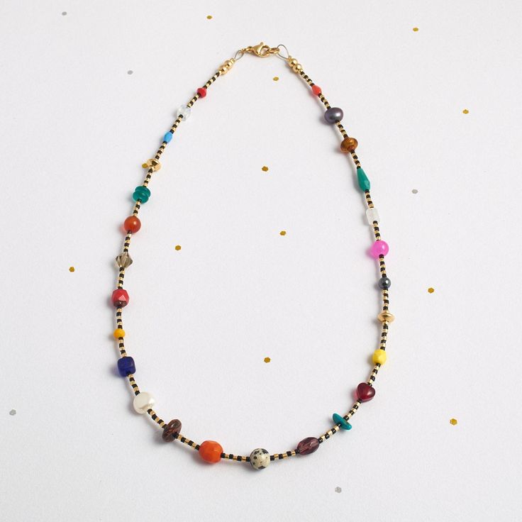 a multicolored beaded necklace on a white surface with confetti sprinkles