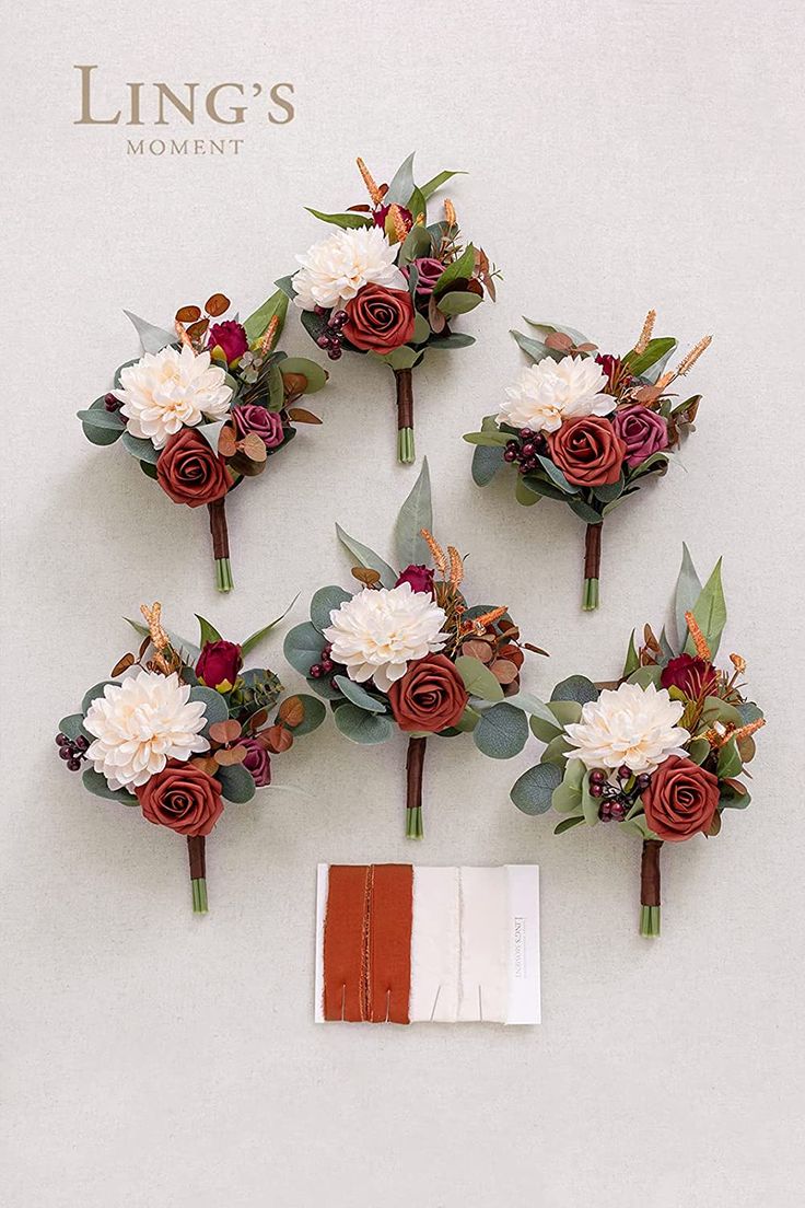 wedding bouquets with flowers and foliage arranged on the wall next to an orange piece of paper