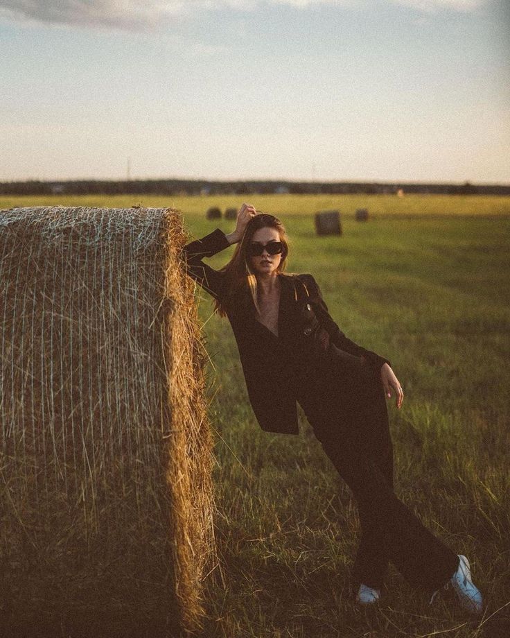 a woman leaning against a hay bale in a field