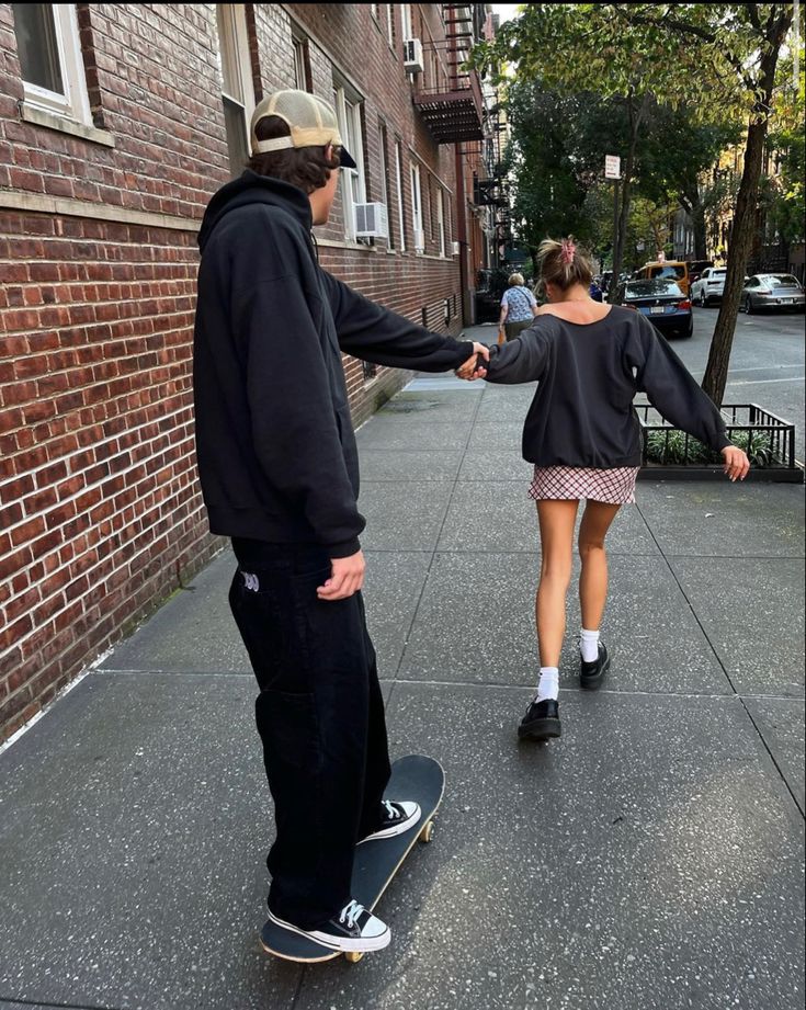 two people are standing on the sidewalk with their skateboards and one person is holding his hand