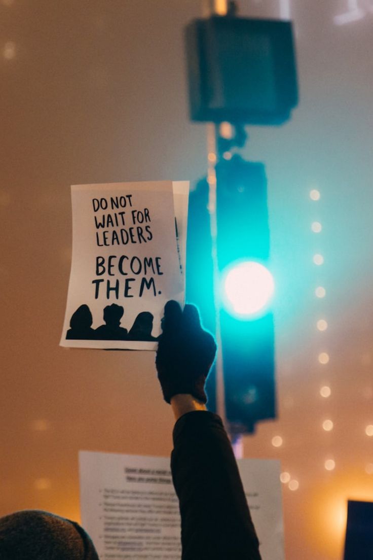 a person holding up a sign that reads do not wait for leaders become them