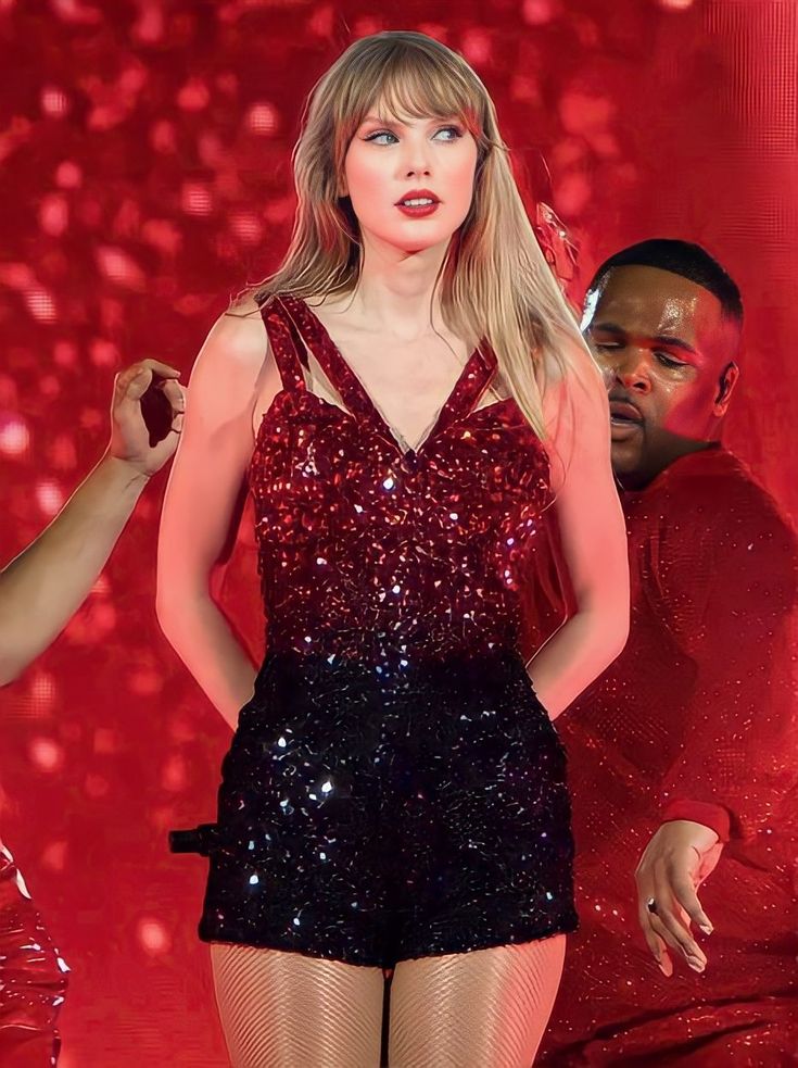 taylor swift performing on stage with two other people in the background wearing red and black outfits