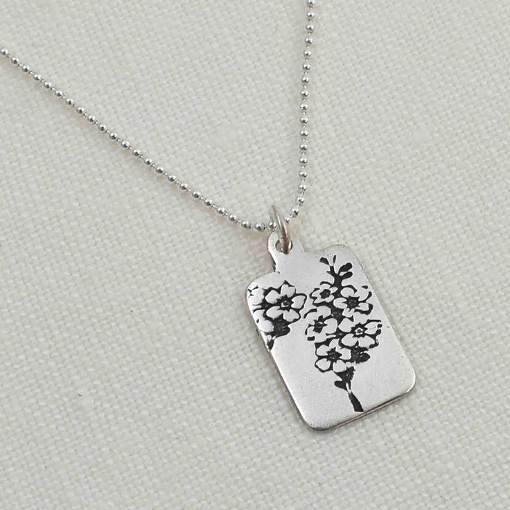 Cherish the memories of those you hold dear with this handcrafted Sterling Silver Forget Me Not Flower Necklace. Featuring an artist-original engraving of the delicate forget me not flower, this pendant is more than just jewelry - it's a heartfelt symbol of remembrance. A black patina enhances every detail of the design, bringing the flower's beauty to life. The rectangular pendant measures approximately 5/8" x 7/16" and hangs from an 18" sterling silver ball chain. Complete your sentimental ens Nature-inspired Jewelry With Flower Charm For Anniversary, Etched Sterling Silver Necklace For Gift, Sterling Silver Etched Necklace For Gift, Etched Sterling Silver Necklace Gift, Nature-inspired Sterling Silver Etched Jewelry, Nature-inspired Etched Sterling Silver Jewelry, Heart Pendant Jewelry With Flower Charm For Anniversary, Anniversary Jewelry Heart Pendant With Flower Charm, Anniversary Heart Pendant Jewelry With Flower Charm