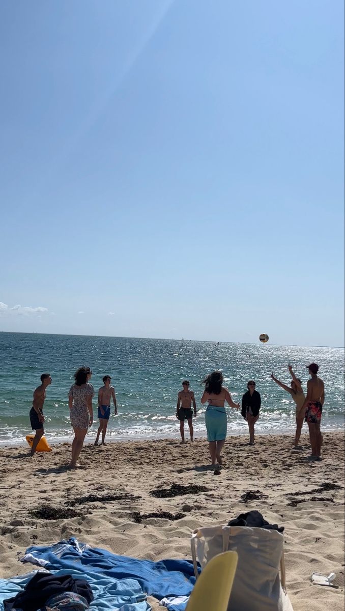 a group of people standing on top of a sandy beach next to the ocean with a frisbee flying in the air