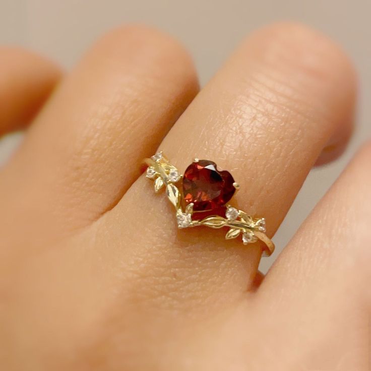 Cue the romance with our stunning Heart’s Desire Red Garnet Ring. This perfect expression of true love features a heart-shaped red garnet center stone along with a curved white topaz leafy band that adds a natural charm. A cherished keepsake that radiates love from every angle. ✦ Available in both 14K yellow gold vermeil (14K yellow gold plated over a sterling silver base) and 10K solid yellow gold. Red Stone Wedding Rings, Heart Shaped Ruby Ring, Garnet Promise Rings, Garnet Heart Ring, Red Rings Engagement, Red Promise Rings, Red And Gold Ring, Heart Stone Ring, Gold Red Jewelry