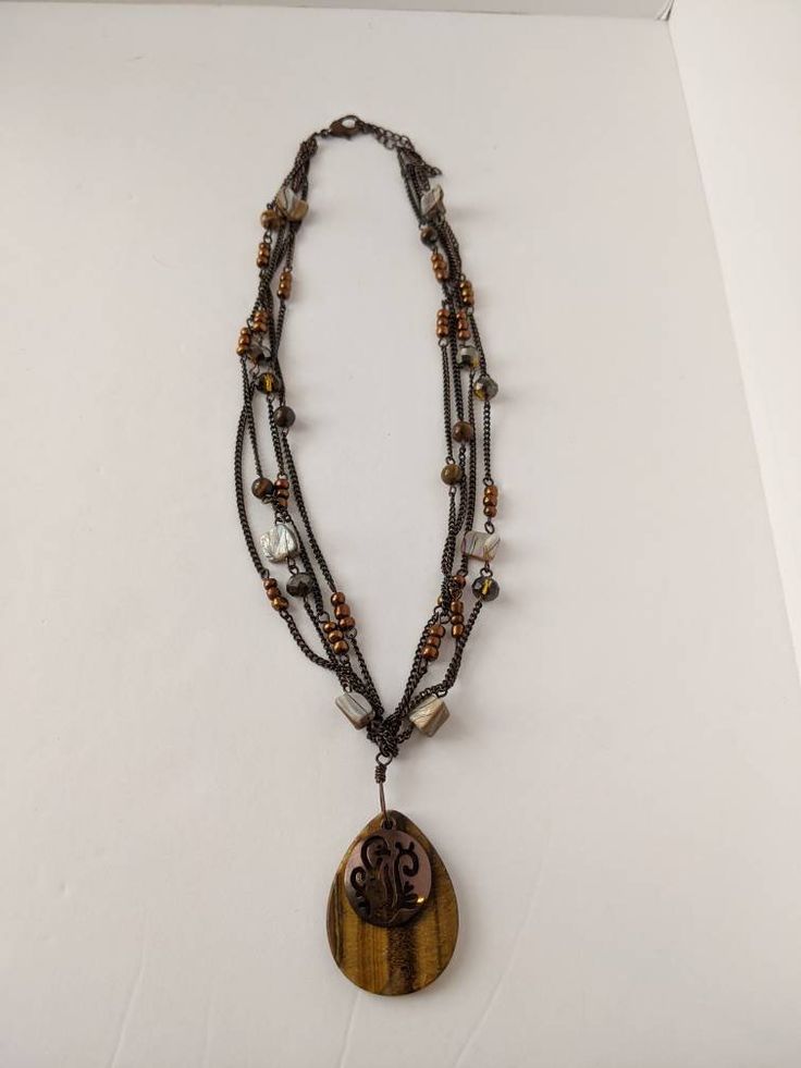 Beautiful vintage boho style necklace. Teardrop shaped tigers eye stone pendant with a filigree cutout copper-tone accent on top. The tigers eye has two small chips along the bottom but they're almost impossible to see. Strung on four antiqued bronze tone chains with pearl shell chips, crystal beads and copper colored faux pearls accents. Pendant measures 1.75 inches long. Necklace is 16 inches long with a lobster claw clasp and 3 inch adjustable chain. Shop Policies: Shipping: All items will be Tigers Eye Stone, Vintage Boho Style, Boho Style Necklaces, Vintage Boho Fashion, Teardrop Pendant, Tiger Eye Stone, Eye Stone, Pearl Shell, Tigers Eye