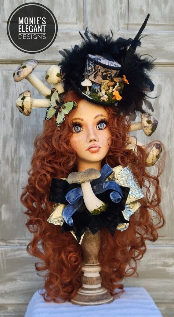 a doll with long red hair and blue eyes wearing a black hat, sitting on top of a table