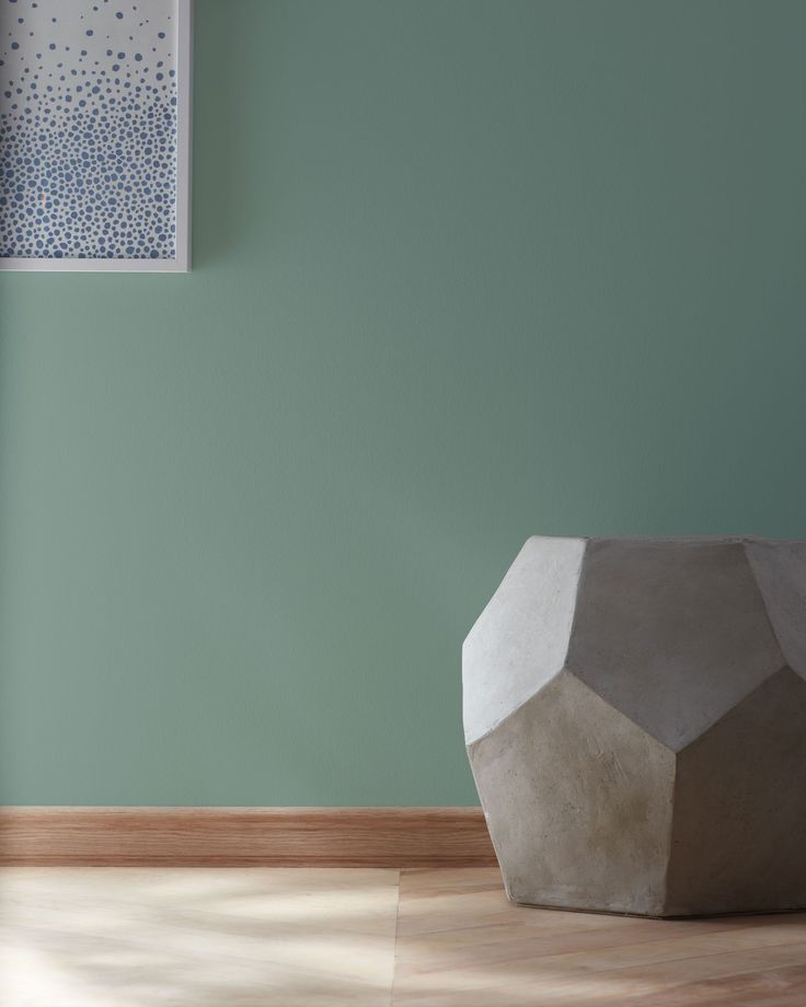 a vase sitting on top of a hard wood floor next to a green painted wall