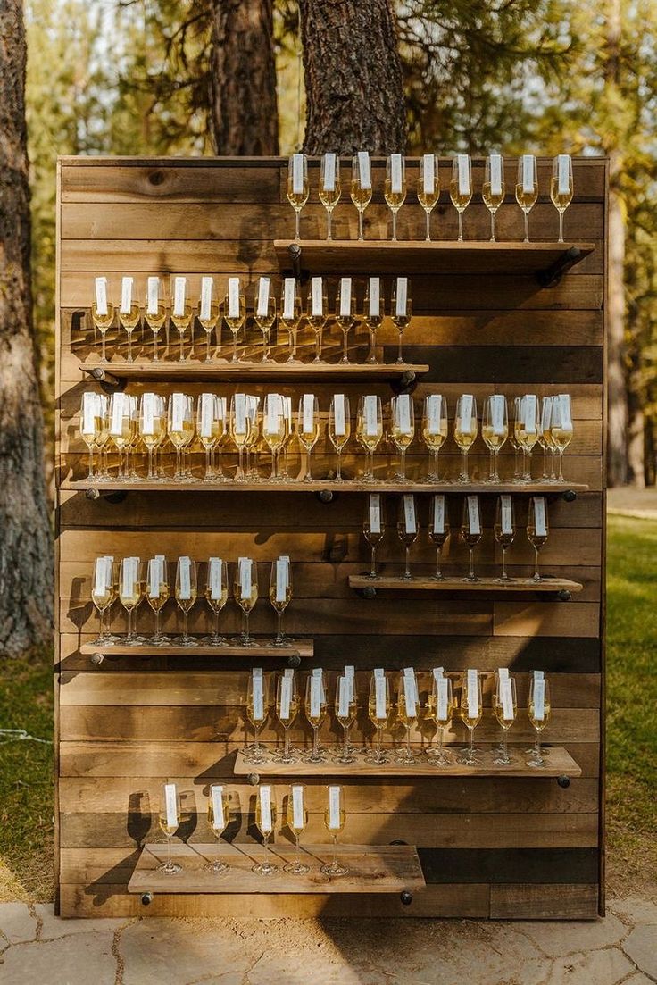 wine glasses are lined up on a wooden shelf in front of some trees and grass