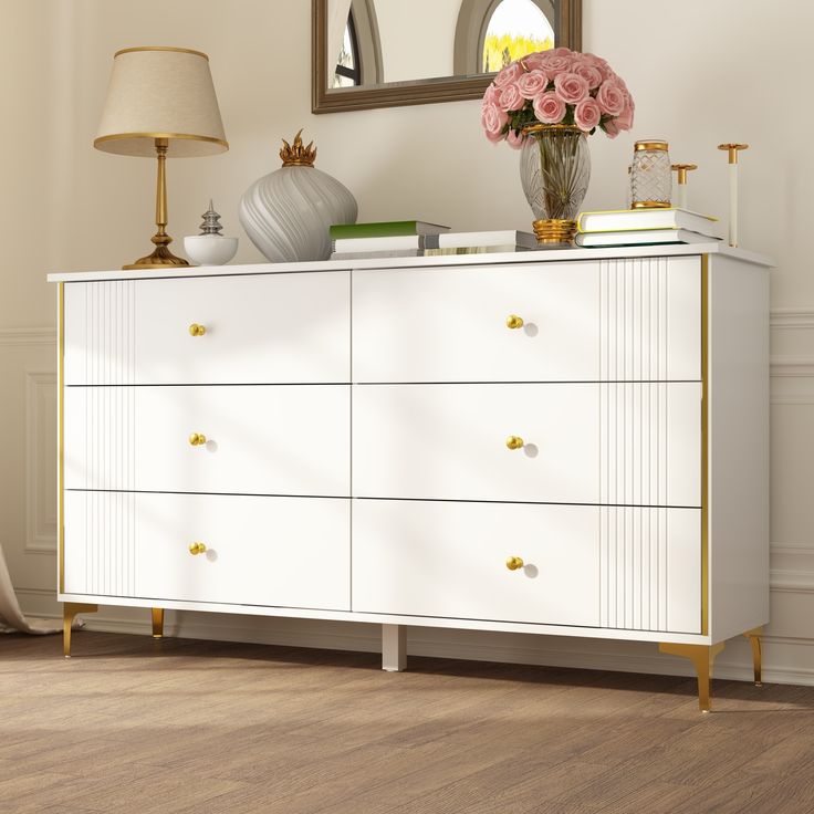 a white and gold dresser with pink flowers on top in a living room next to a mirror