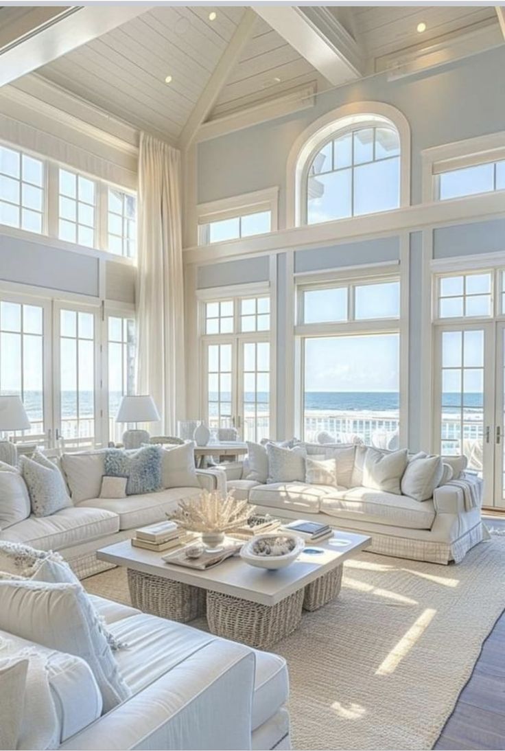 a living room filled with lots of white furniture next to large windows on top of a wooden floor