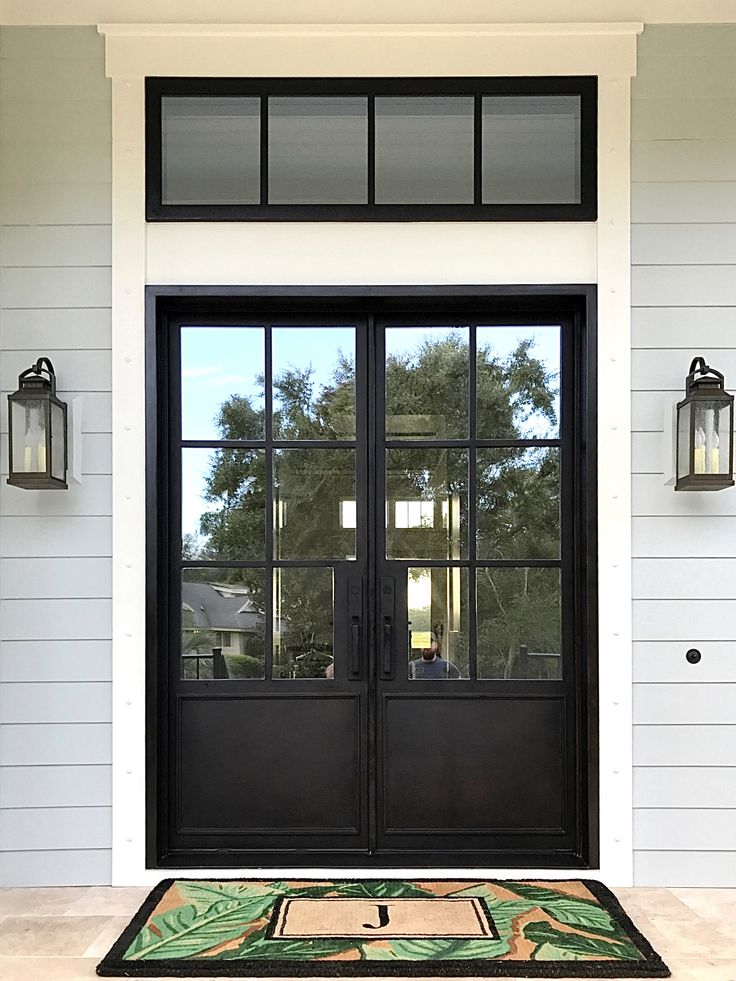 a black double door with two lanterns on either side and an area rug in front