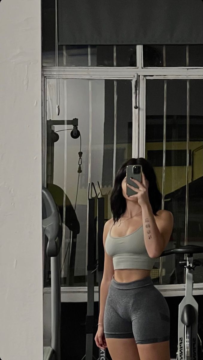 a woman taking a selfie in front of a gym mirror with her cell phone