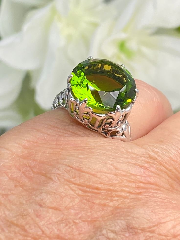 Peridot Sterling Silver RingKing Design#D123 This is a reproduction of a sterling silver Gothic filigree antique ring with a stunning 12 carat green peridot gemstone solitaire. This round cut simulated gem is 15mm in diameter. The inside of the band is marked 925 for sterling silver. Notice the beautiful intricate Gothic claw design of the silver filigree setting. The swirls echo down the band. This large round gemstone sits regally atop the fashionable setting. This stately ring garners attenti Green Ring With Large Stone, Formal Green Ring With Large Stone, Classic Green Jewelry With Large Stone, Classic Silver Peridot Rings, Classic Silver Ring With Peridot, Classic Peridot Jewelry For May Birthstone, Classic Green Gemstone With Center Stone, Elegant Green Peridot Gemstones, Classic Peridot Jewelry With Accent Stones