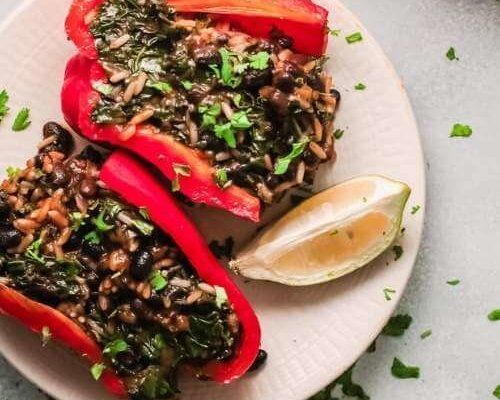 two stuffed peppers are on a plate with rice and vegetables next to a lemon wedge