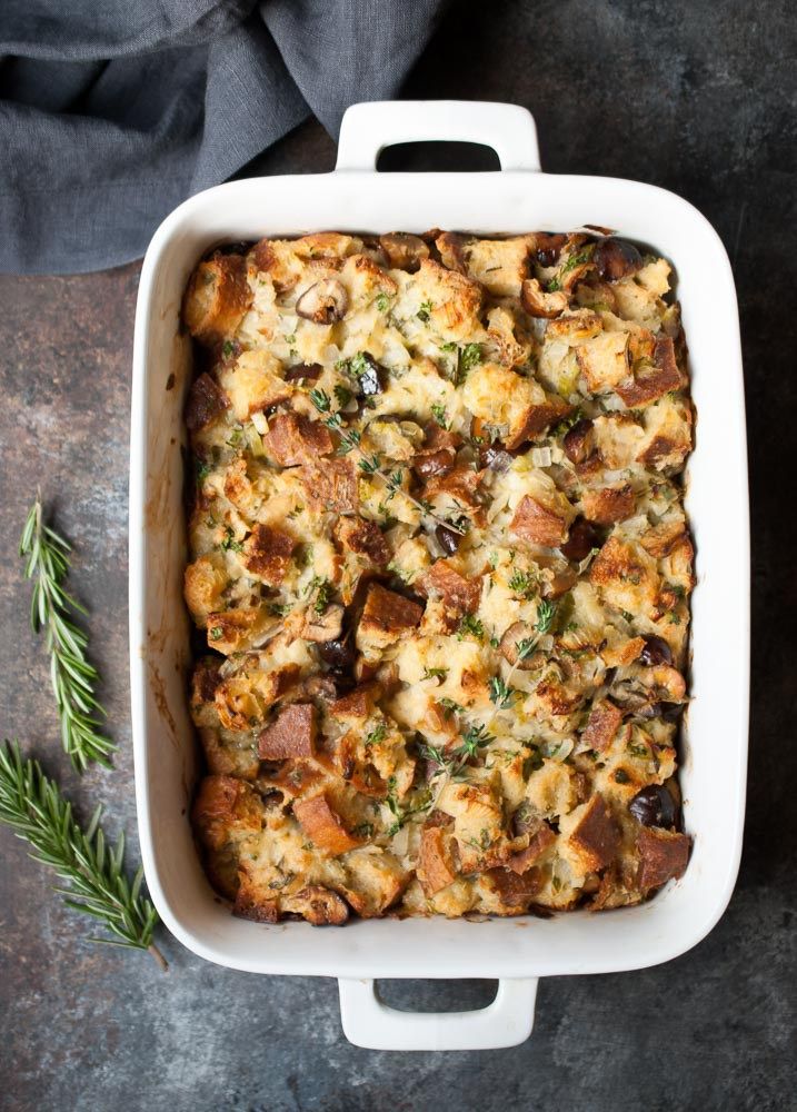 a casserole dish with meat and vegetables in it on a gray surface next to a sprig of rosemary