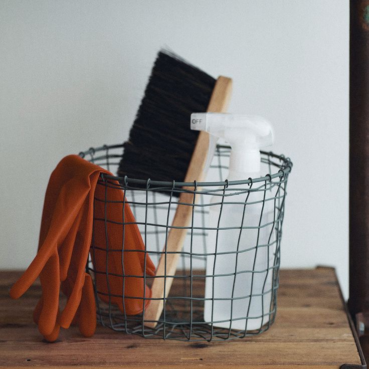 a metal basket with two orange gloves and a brush in it on a wooden table