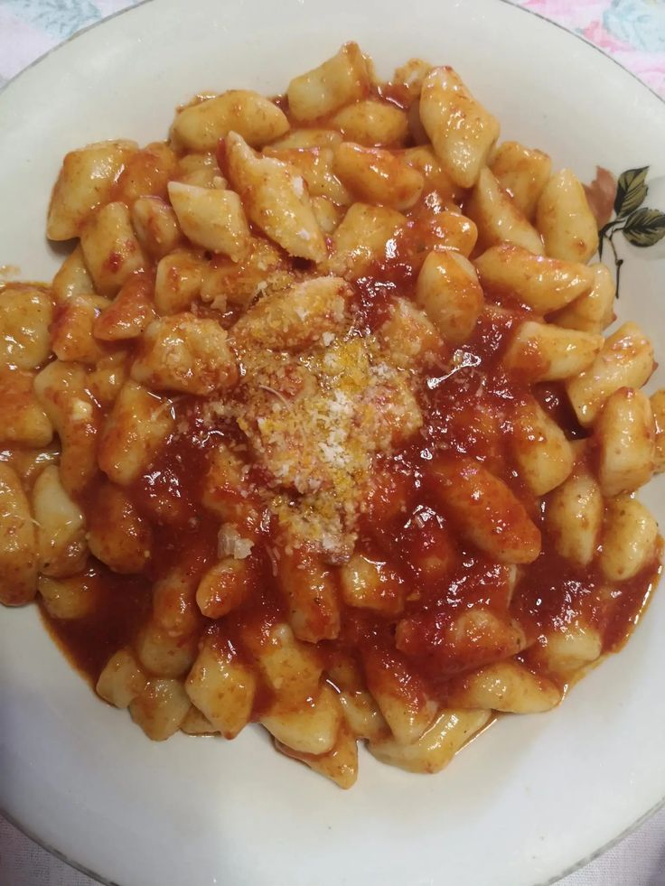 a white plate topped with macaroni and cheese covered in marinara sauce on top of a pink table cloth