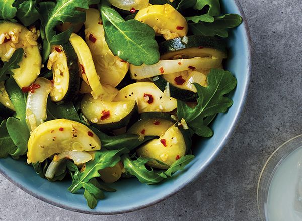 a blue bowl filled with spinach and other vegetables next to a glass of water