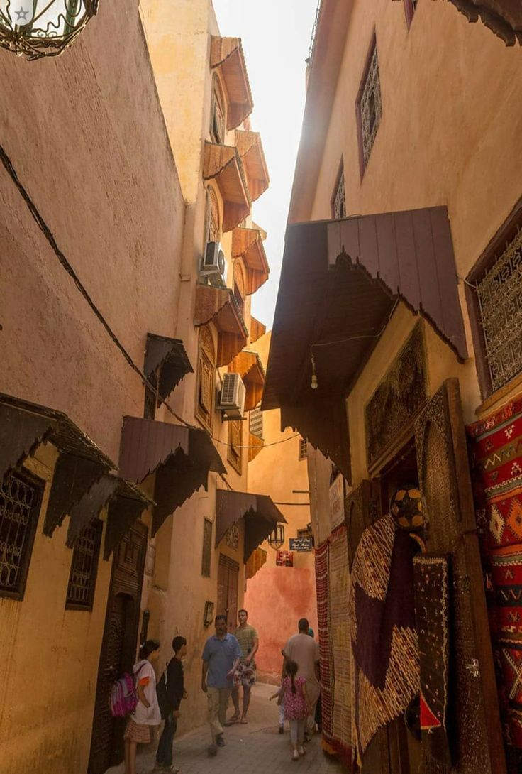 several people are walking through an alleyway in the old part of town, with shops on either side