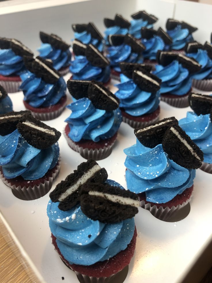 cupcakes decorated with blue frosting and black graduation caps are on a white tray