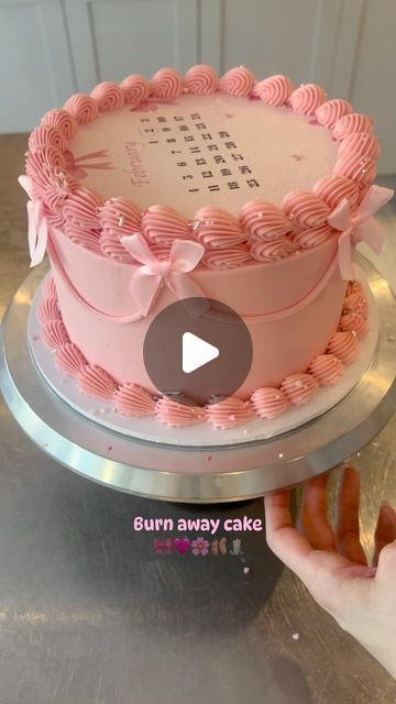 a pink cake sitting on top of a metal counter next to a person's hand