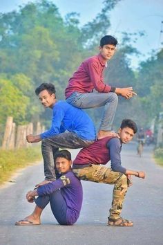 four young men are standing on one another in the middle of an empty road with trees behind them