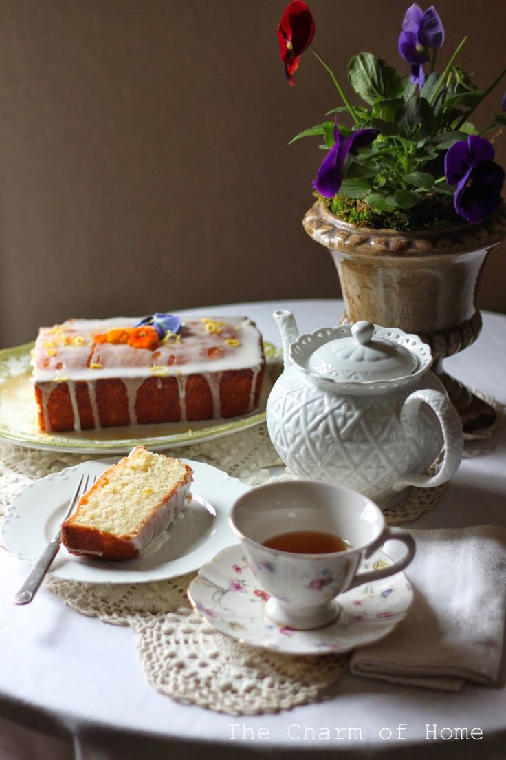 a table topped with cake and tea cups filled with liquid next to a potted plant