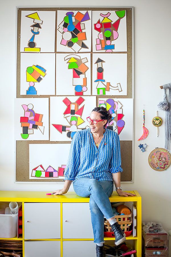 a woman sitting on top of a yellow table in front of a wall with paintings