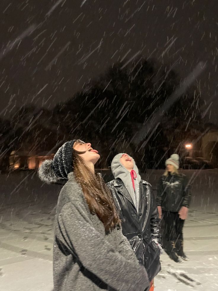 two people are standing in the snow and one is looking up at something with his eyes closed