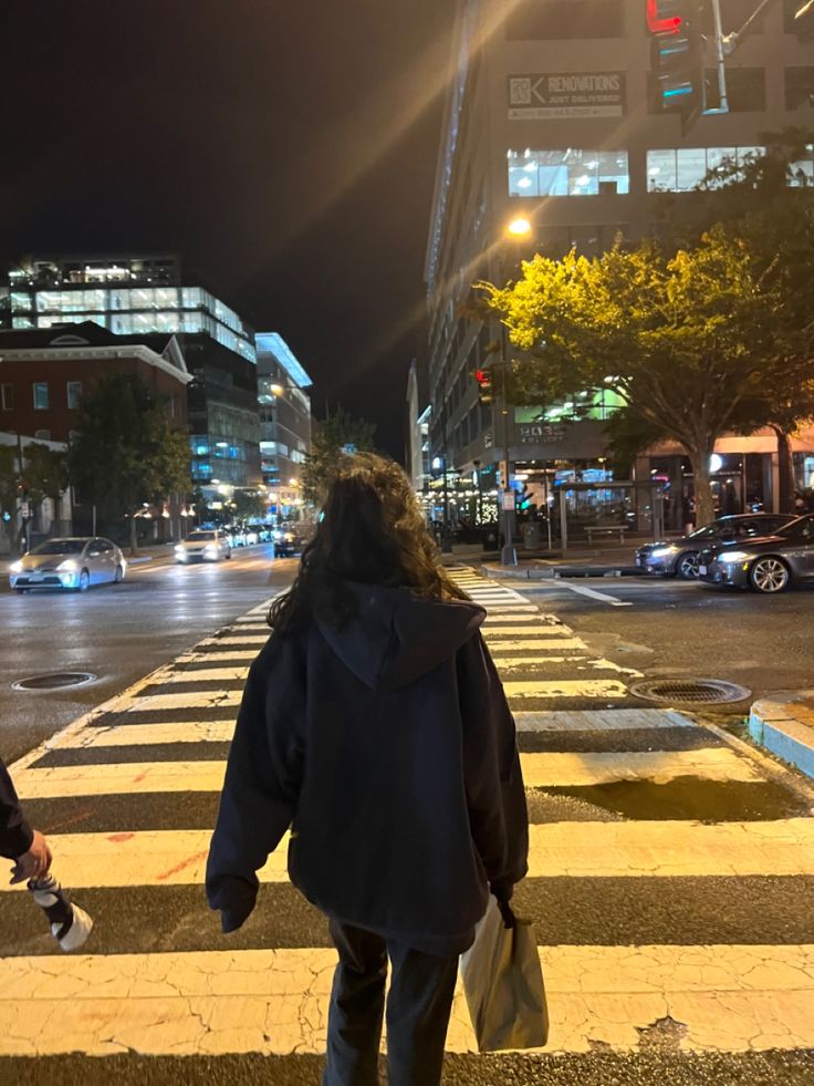 a woman walking across a cross walk at night