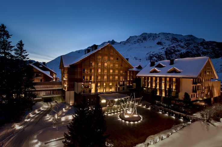 the hotel is lit up at night in front of snowy mountains