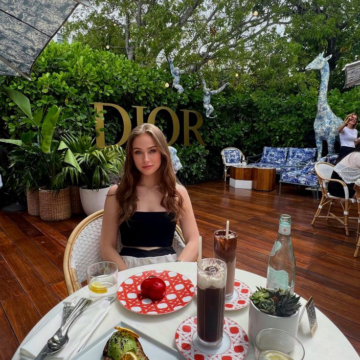 a woman sitting at a table with food and drinks on it in front of her