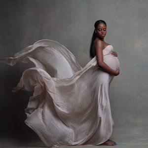 a pregnant woman in a white dress is posing for a photo with her flowing fabric