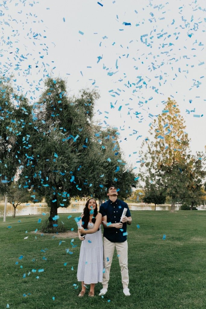 a man and woman standing in front of a tree surrounded by blue confetti