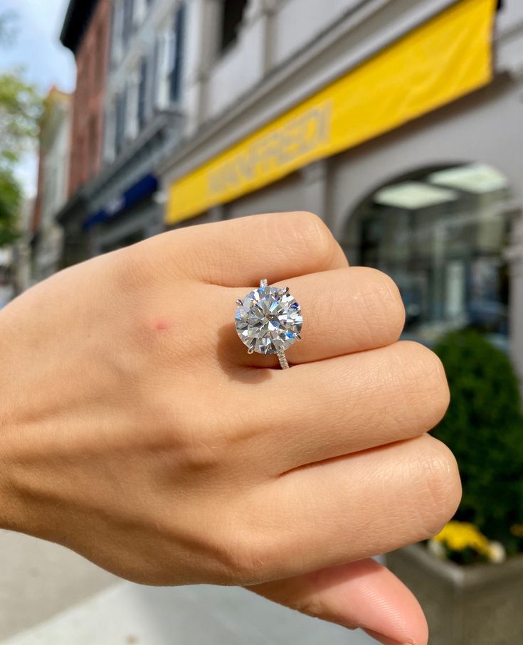 a woman's hand holding a diamond ring in front of a store on the street