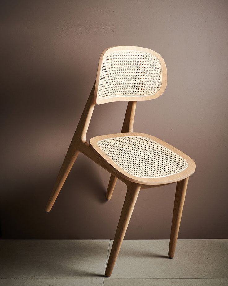 a wooden chair sitting on top of a cement floor next to a brown wall with a shadow