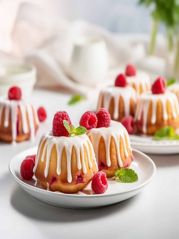 three small desserts with raspberries and icing on them sitting on plates