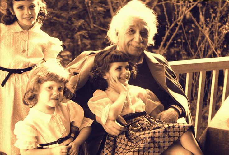 an old black and white photo shows three children in dresses, one older woman sitting on a bench