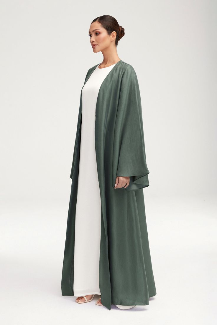 Transform any outfit into a statement with our Seema Flare Sleeve Open Abaya in Dark Forest. Its luxurious fabric boasts a subtle sheen, while the dramatic flare sleeves add a touch of artful elegance. Step out in style and sophistication with this exclusive piece. Model is 5'7" and is wearing size XS/58". Elegant Flowy Spring Abaya, Elegant Abaya With Kimono Sleeves For Eid, Eid Abaya With Kimono Sleeves And Elegant Style, Eid Elegant Abaya With Kimono Sleeves, Flowy Long Abaya For Eid, Elegant Flowy Abaya For Eid, Elegant Abaya With Cape Sleeves, Elegant Cape Kaftan For Eid, Elegant Kimono With Kimono Sleeves For Eid