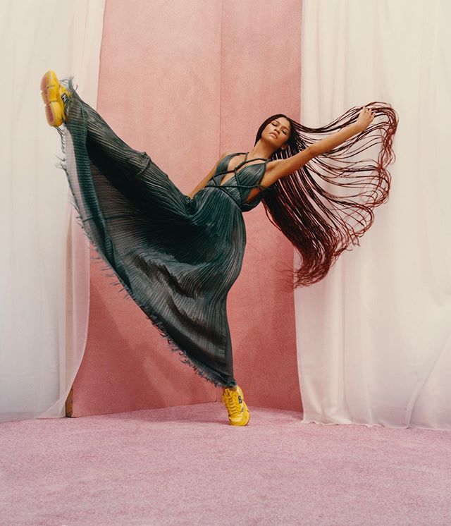 a woman with long hair and yellow shoes is dancing in front of white drapes