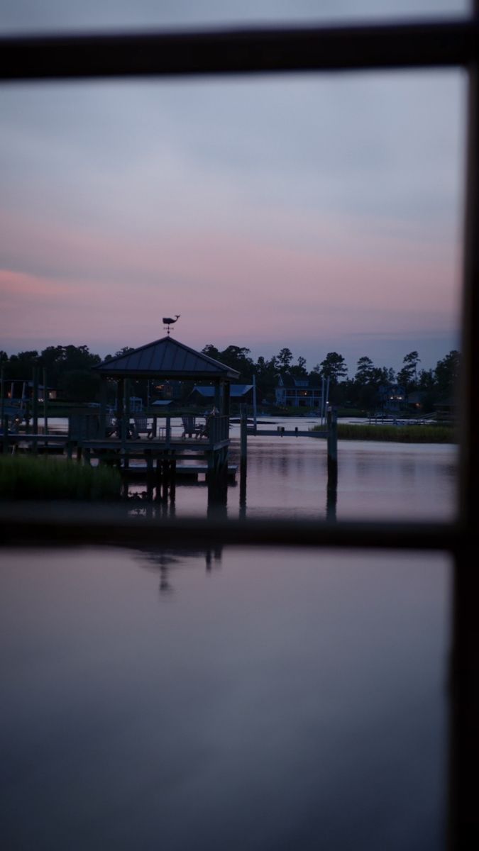 the water is reflecting the dock at dusk, as seen through a window with a view