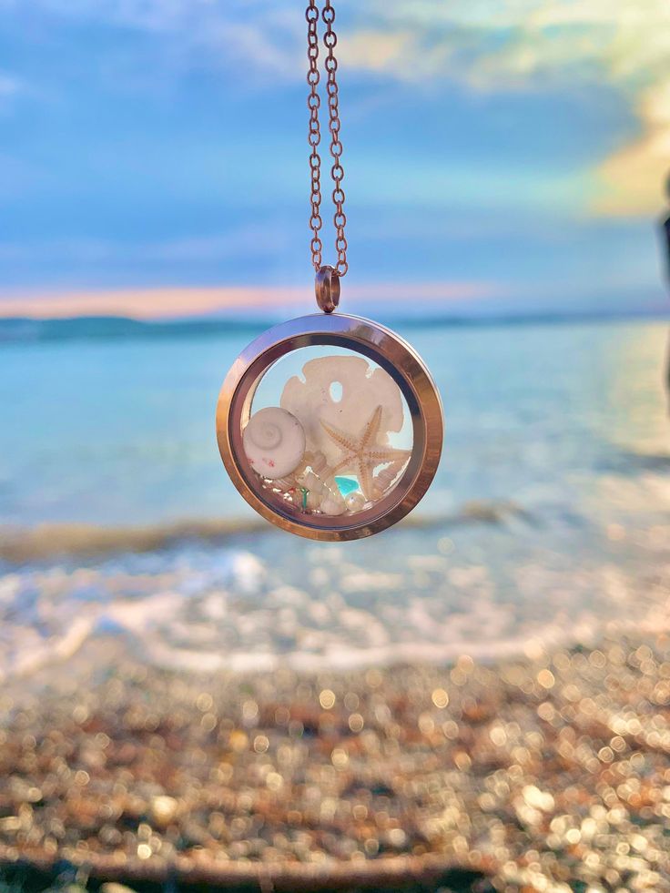 a close up of a clock on a chain near the water and sand at the beach