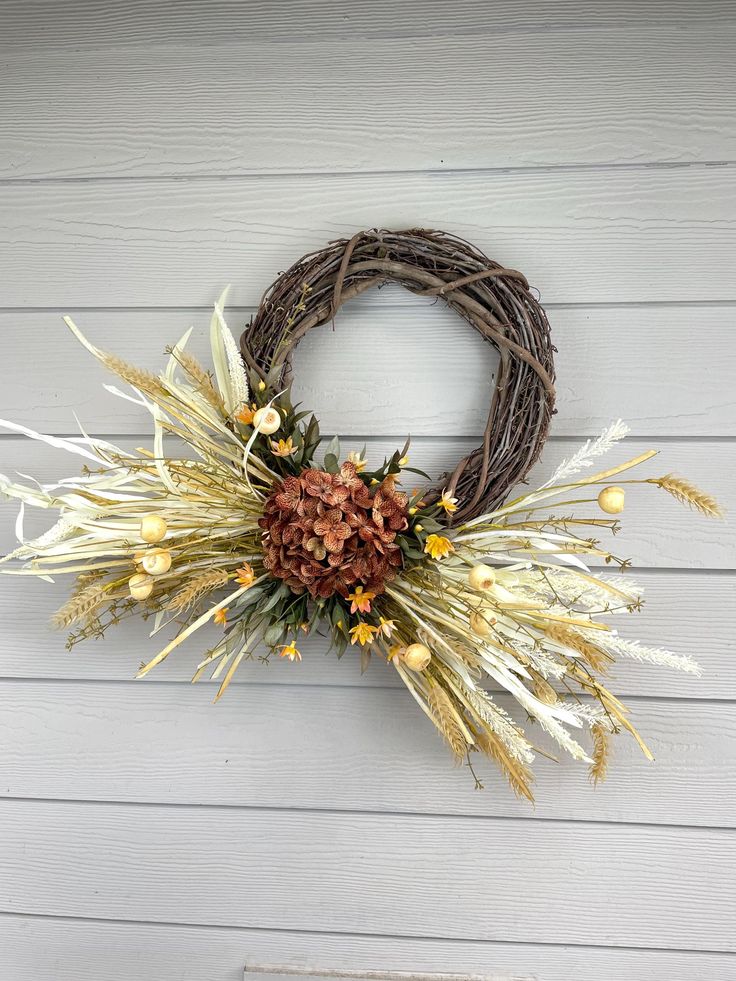 a wreath hanging on the side of a building with dried flowers and leaves around it